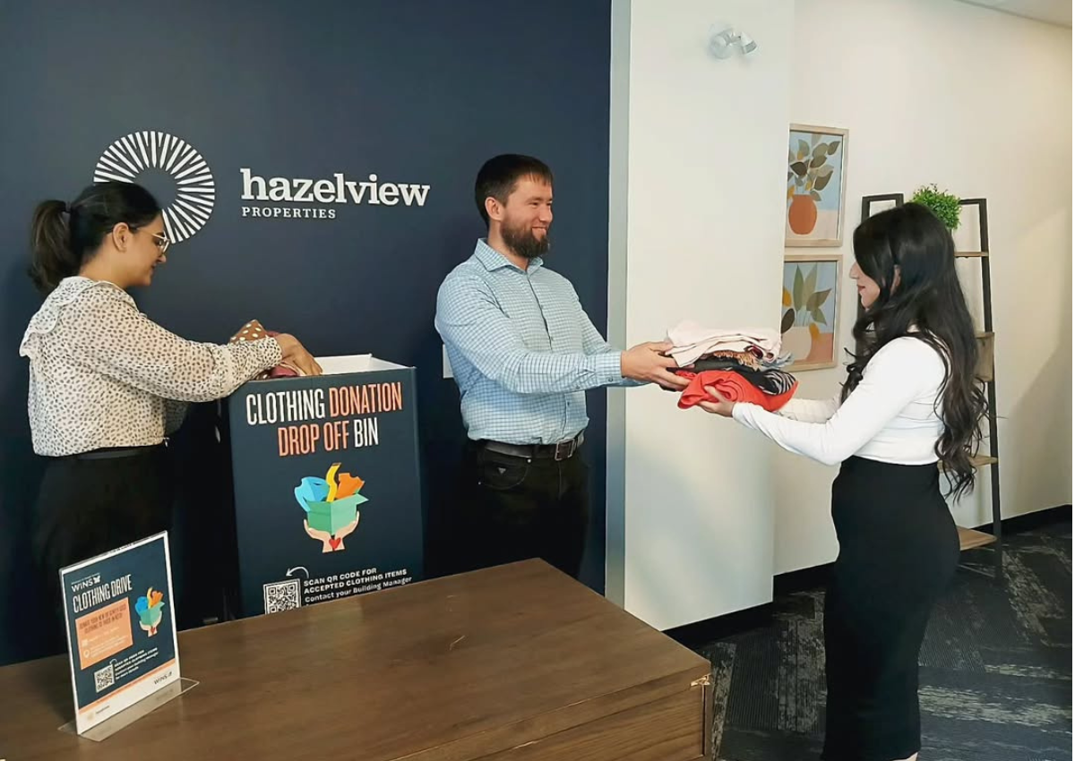 People donating folded clothing at a drop‑off bin inside a Hazelview Properties office.