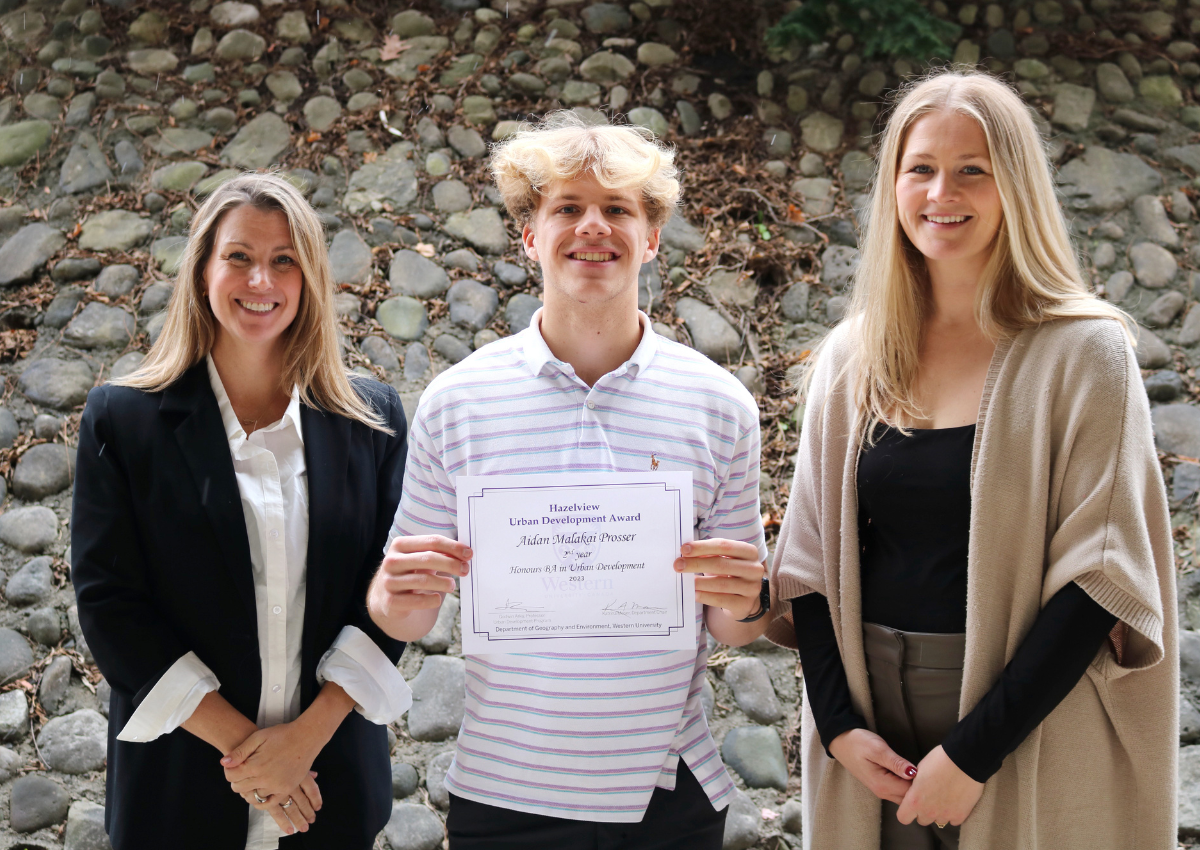 Three people standing outdoors, with one holding a certificate.