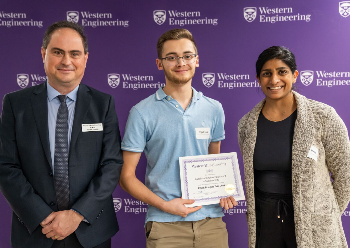 Three people standing in front of a Western Engineering backdrop, one holding a certificate.