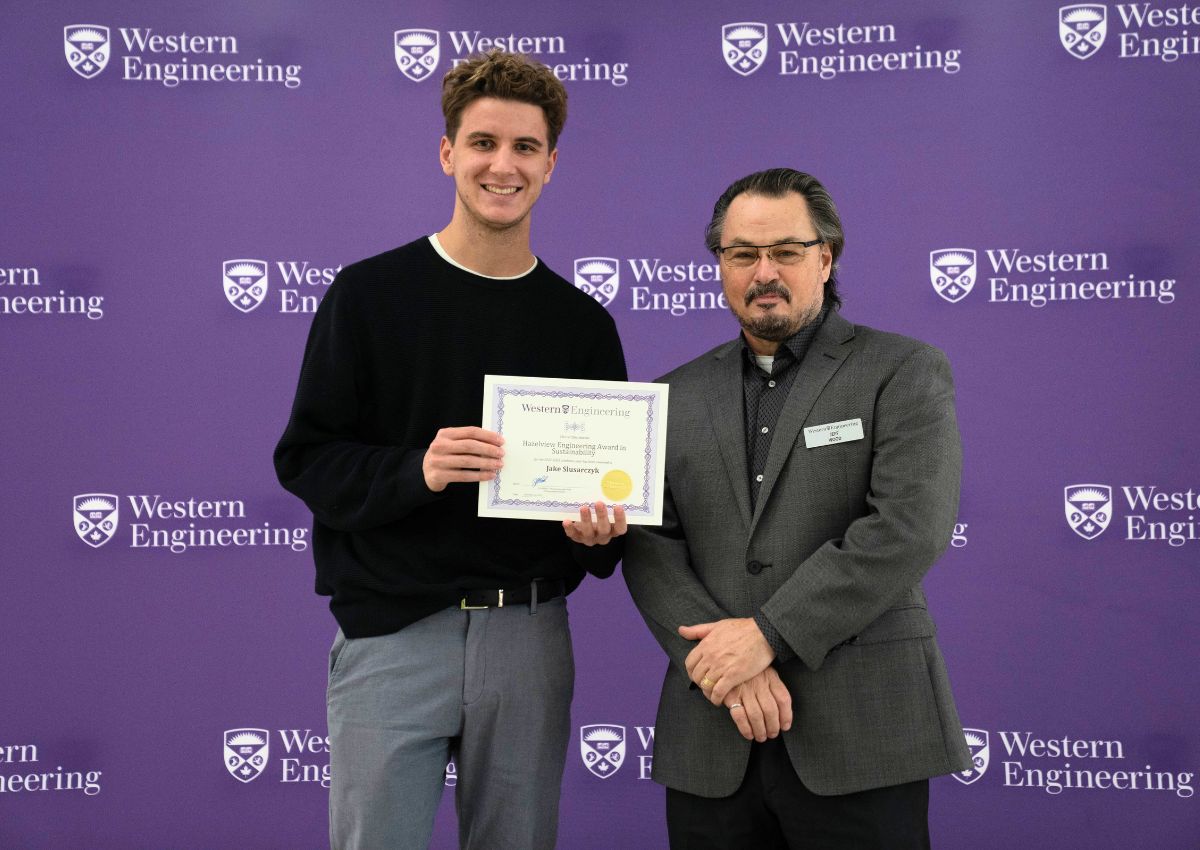 Two people standing in front of a Western Engineering backdrop, one holding a certificate.