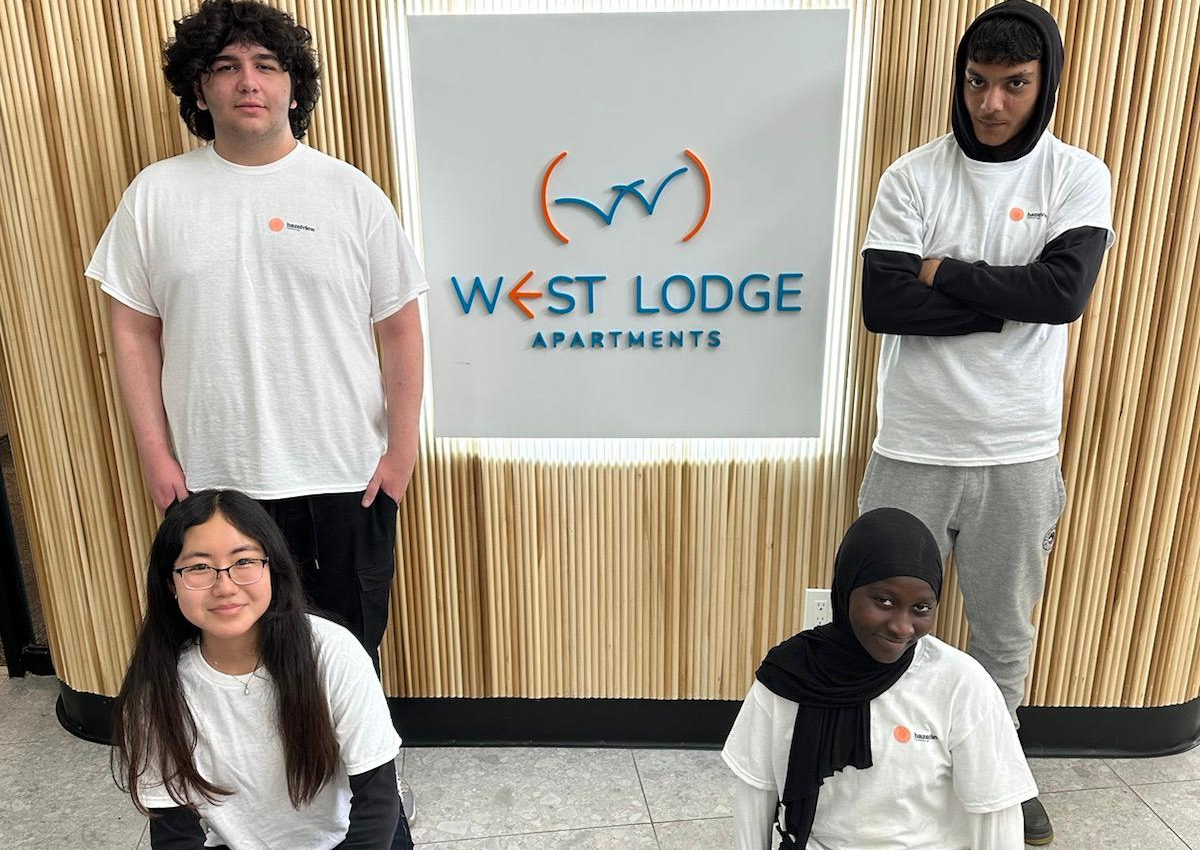 Four people standing in front of a sign reading ‘West Lodge Apartments’.